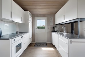 A narrow kitchen with white cabinets, a built-in oven, and a window with a view of greenery.