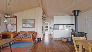 A cozy living room with a sofa, a dining table, a fireplace, and a kitchen in the background. - Beautiful sunsets 100 meters from the beach (Brenderup)