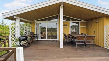 A covered outdoor area with a wooden deck, a grill, and outdoor furniture.