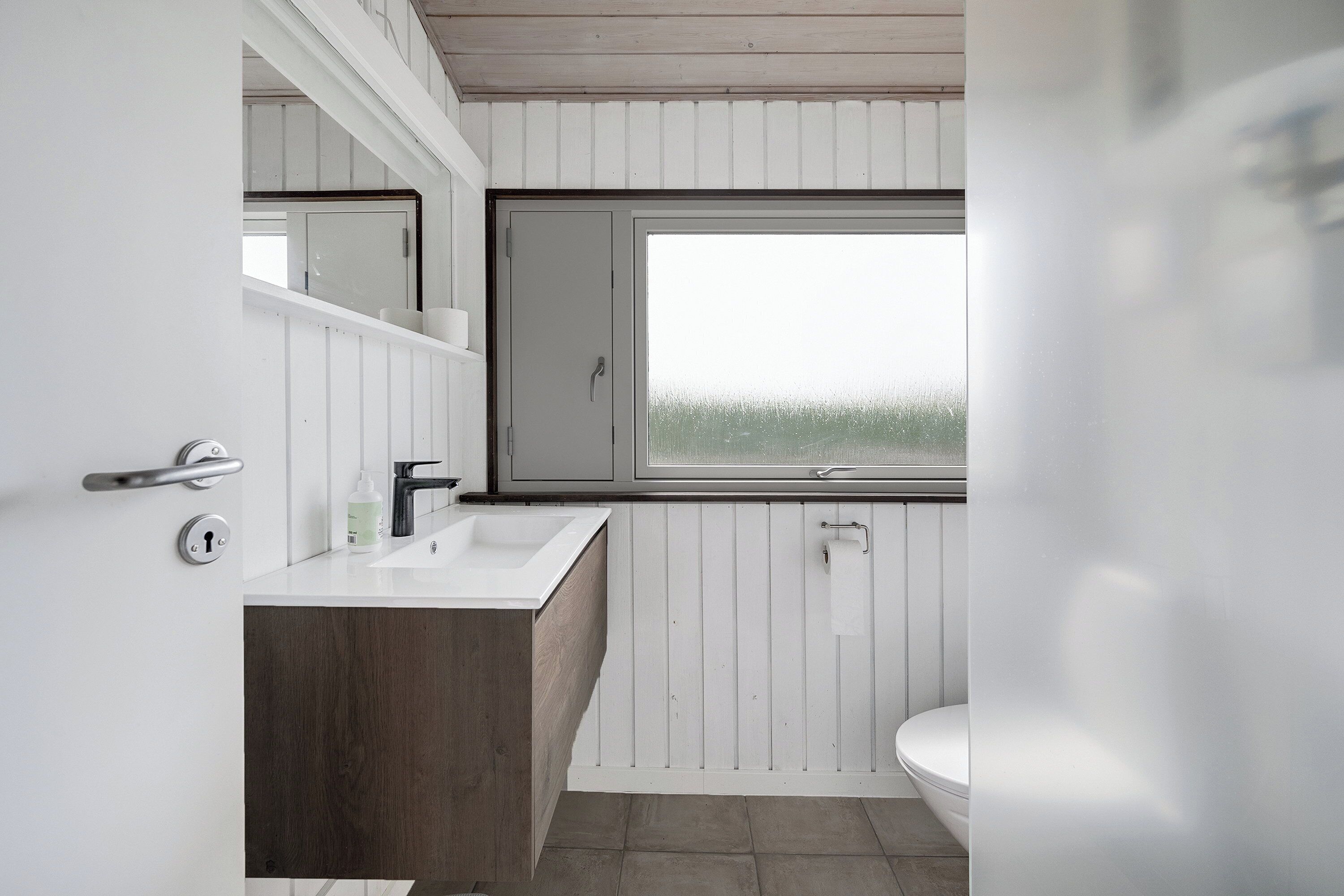 A bathroom with a wooden vanity, a white sink, a mirror, and a window.