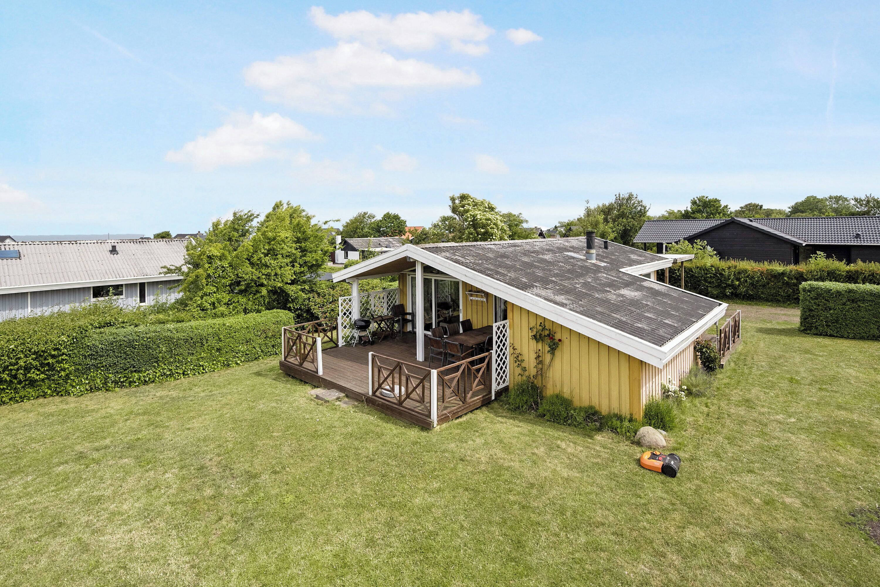 Einbungalow mit einer Terrasse, umgeben von einem gepflegten Rasen und Hecken.
