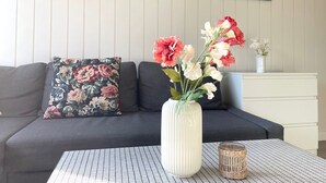 A living room with a sofa, a floral pillow, a vase with flowers, a small table, and a wall with paintings. - DA25/1 - Family-friendly, comfortable vacation apartment with garden use - House (Cuxhaven)