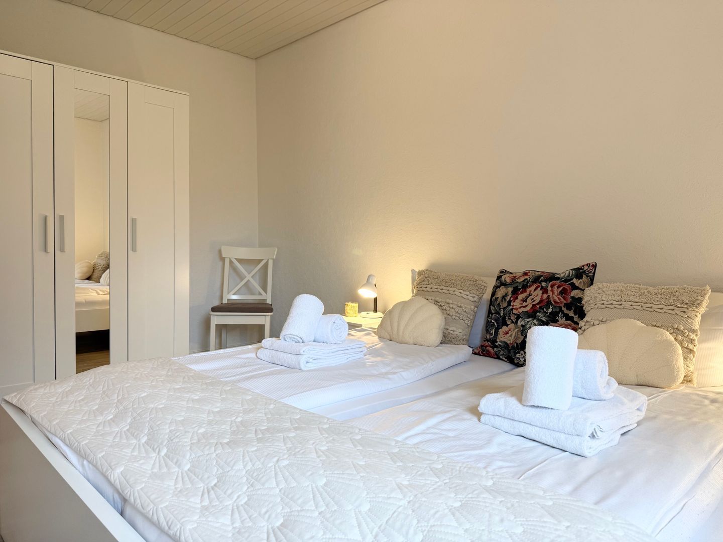 Ein Schlafzimmer mit einem großen Bett, einem Kleiderschrank, einem Sessel und einem Nachttisch mit Lampe.