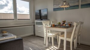 A dining area with a table, chairs, a TV, and a radiator. - DA25/1 - Family-friendly, comfortable vacation apartment with garden use - House (Cuxhaven)