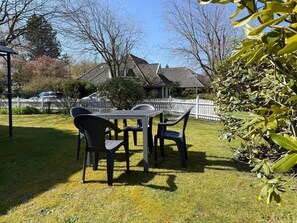 A patio with a table and chairs, a white picket fence, and a house with a tiled roof in the background. - DA25/1 - Family-friendly, comfortable vacation apartment with garden use - House (Cuxhaven)