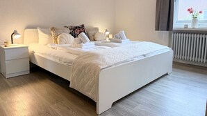 A neatly made bed with white linens and towels, a bedside lamp, and a window with a view of flowers. - DA25/1 - Family-friendly, comfortable vacation apartment with garden use - House (Cuxhaven)