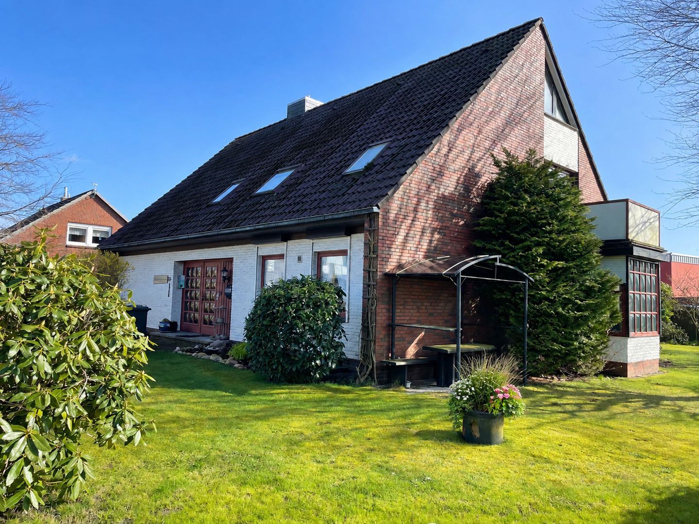 Ein zweistöckiges Haus mit geneigtem Dach, einer Ziegel Fassade und einem kleinen Garten mit Rasen und Topfpflanzen.