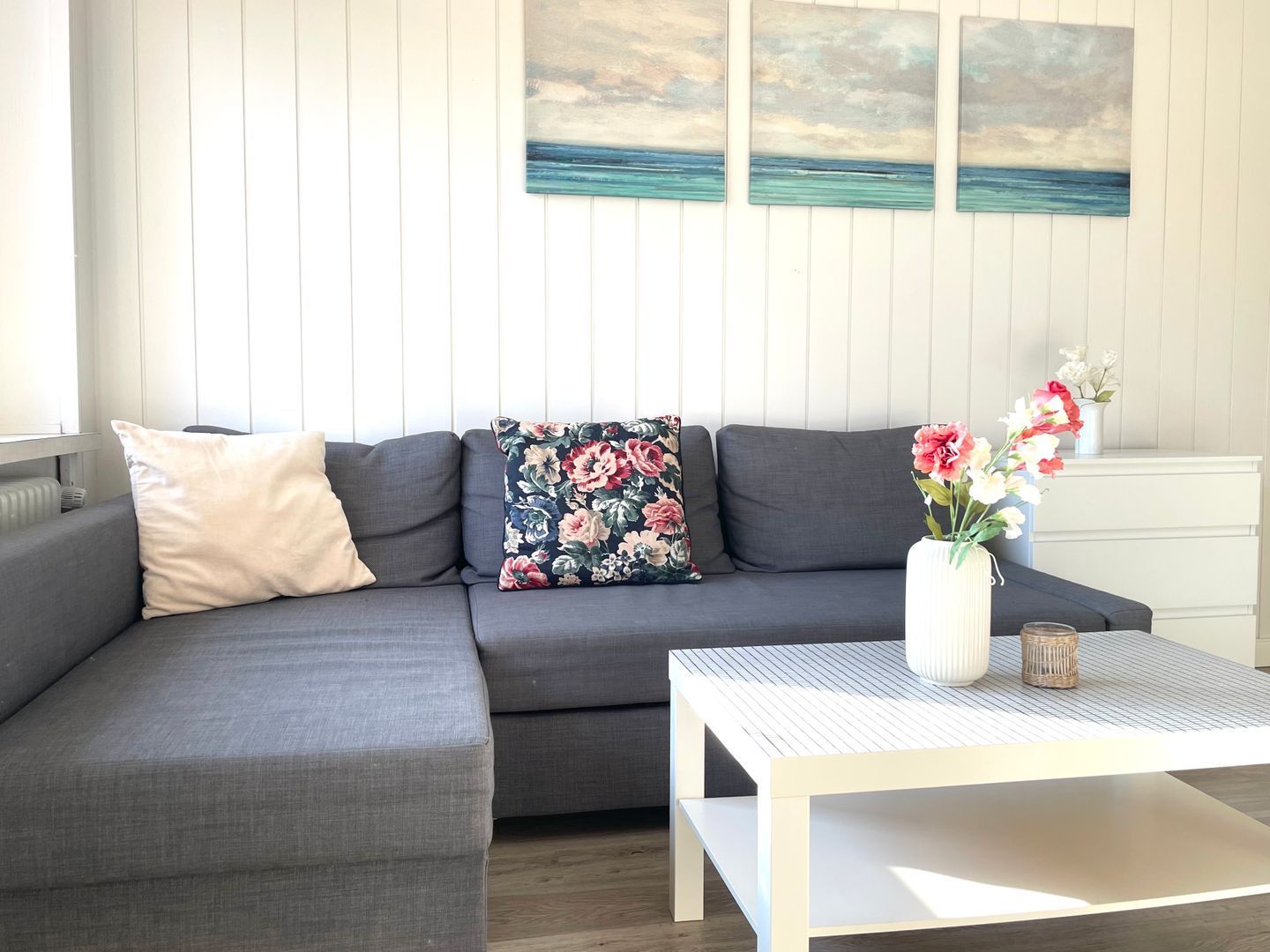 A modern living room with a grey sectional sofa, a white coffee table, and a floral pillow.