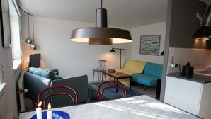 A modern living room with a sofa, a dining table with candles, and a kitchen area. - Cozy apartment in old farm (Svaneke)