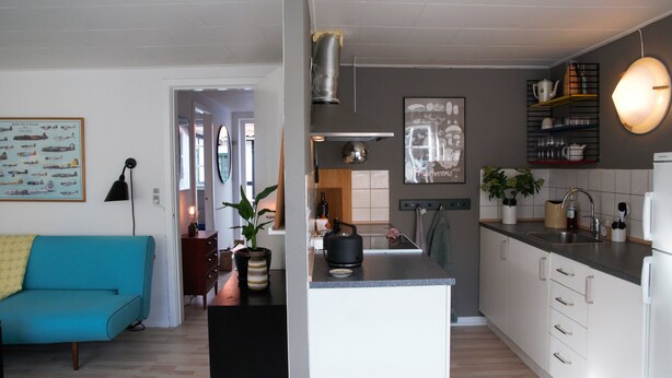 A modern kitchen with a central island, white cabinets, and a dining area with a blue sofa. - Cozy apartment in old farm (Svaneke)