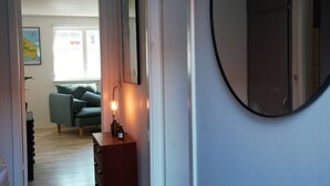 A hallway with a sofa, a small table with a lamp, a framed picture, and a round mirror. - Cozy apartment in old farm (Svaneke)