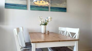 Un coin repas avec une table en bois, des chaises blanches, un vase de fleurs et une suspension.