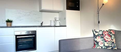 A modern kitchen with white cabinetry, a built-in oven, a coffee maker, and a microwave.