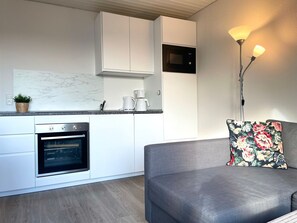 Una cocina moderna con muebles blancos, horno empotrado, cafetera y microondas.