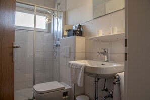 Un baño con ducha, inodoro, lavamanos y perchero para toallas.