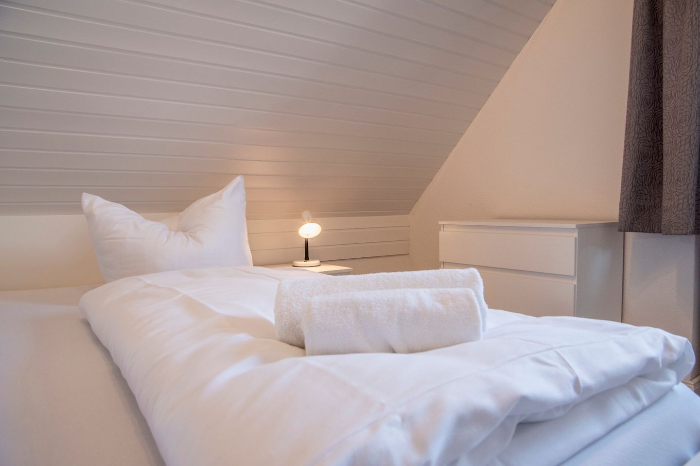 Un lit bien fait, avec du linge de lit blanc, une lampe de chevet et une tête de lit.