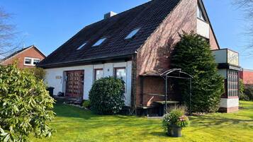 Ein zweistöckiges Haus mit geneigtem Dach, einer Ziegel Fassade und einem kleinen Garten mit Rasen und Topfpflanzen.
