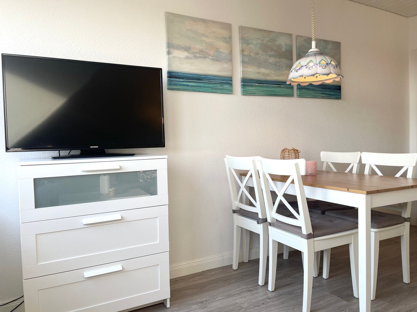 Ein Essbereich mit Fernseher, weißen Möbeln und Bildern an der Wand.
