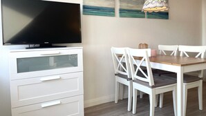 A dining area with a TV, white furniture, and artwork on the wall.
