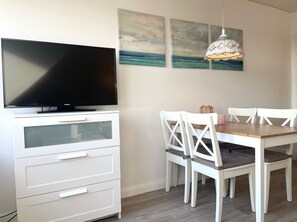 Un comedor con televisión, muebles blancos y obras de arte en la pared.
