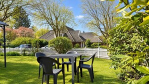 A well-maintained lawn with a dining table and chairs, surrounded by a white picket fence and lush greenery.
