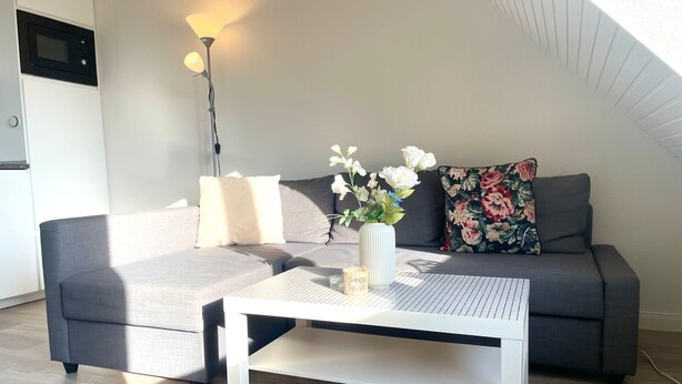 A modern living room with a grey sofa, a white coffee table, a floor lamp, and a vase with flowers.