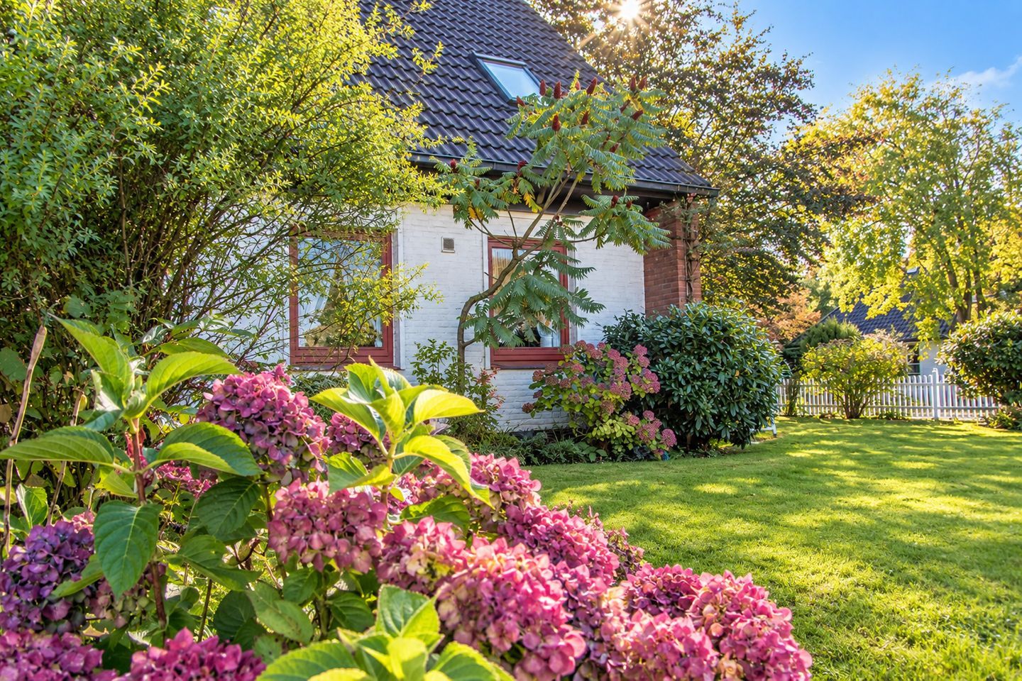 Ein Haus mit geneigtem Dach, umgeben von üppigem Grün und blühenden Pflanzen.