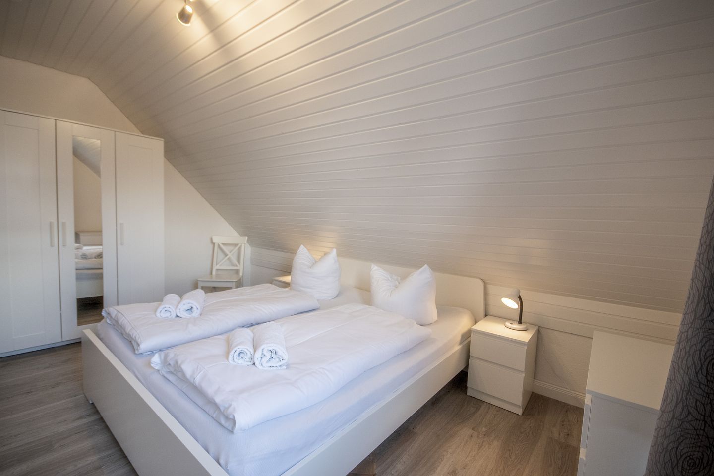 A bedroom with two beds, a nightstand, a chair, and a wardrobe.