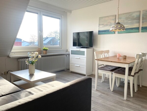 Una sala de estar acogedora con sofá, mesa de comedor con sillas, televisor y ventana con vistas a casas.