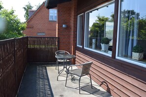 A balcony with two chairs, a table, and a view of a brick building and greenery.