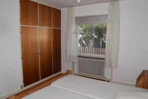 A bedroom with a wooden wardrobe, a window with curtains, a radiator, and a bed.