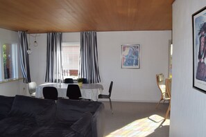 A room with a wooden ceiling, a dining table with chairs, a sofa, and a framed picture on the wall.