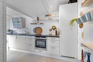 Una cocina moderna con armarios blancos, horno empotrado, lavamanos y encimera con diversos utensilios de cocina.