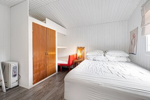 A bedroom with a bed, a wooden wardrobe, a chair, a table with a lamp, and a heater. - Cozy family home near beach and forest (Højby)