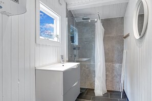 Une salle de bain avec une douche, un lavabo et une fenĂȘtre.