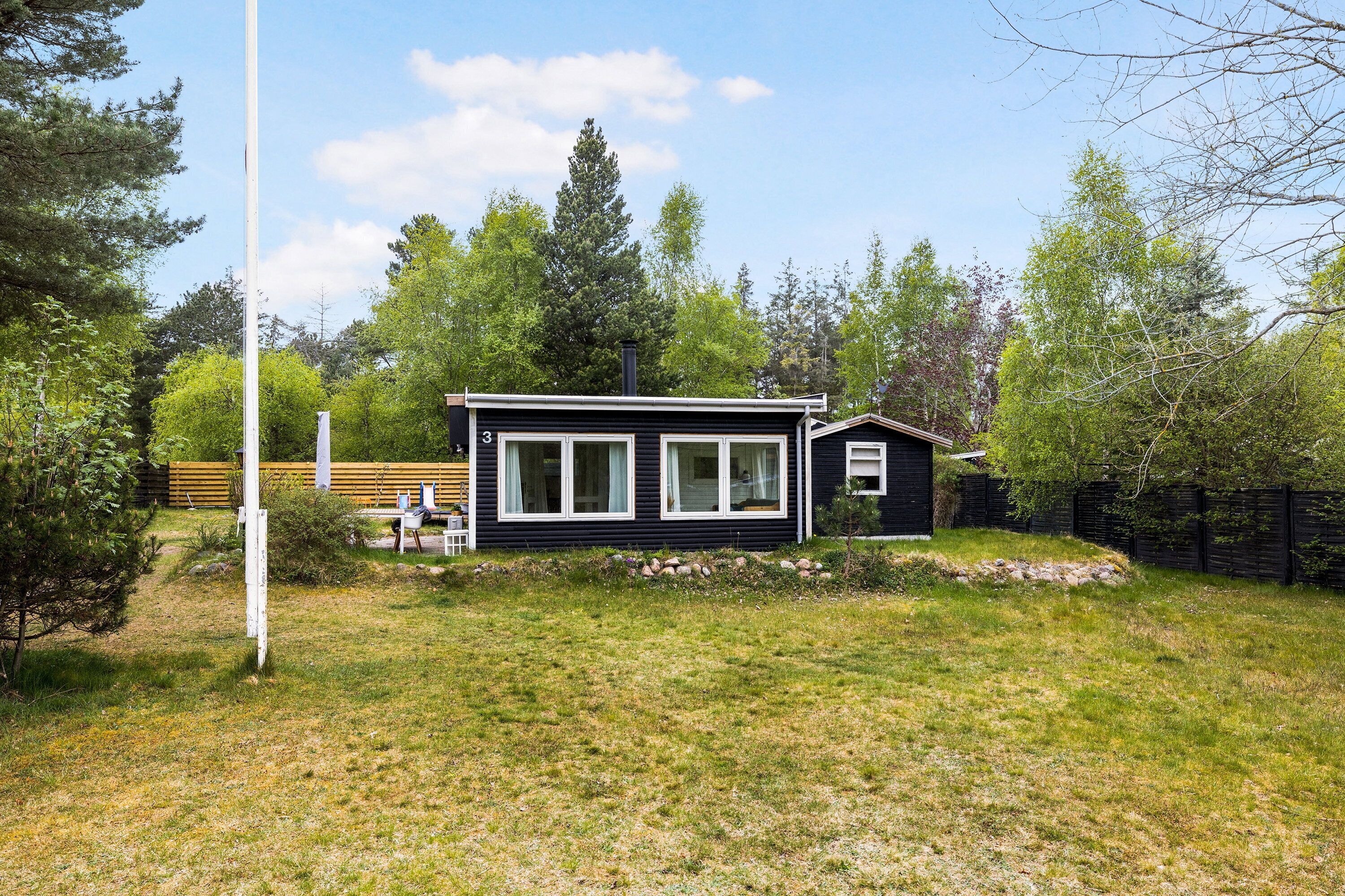 A small black cabin with white trim, a grassy yard, and a wooden fence.