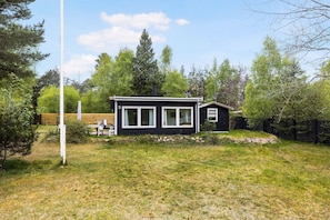 Eine kleine schwarze Holzhütte mit weißem Zierleisten, einem Rasen und einem Holzzaun.