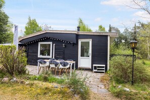 A small black building with a white door, two windows, a bench, and a table with chairs outside. - Cozy family home near beach and forest (Højby)