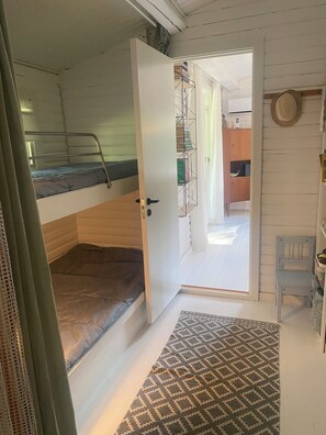 Una habitación con una cama litera, una puerta blanca que da a un pasillo, un tapete estampado y un sombrero en la pared.