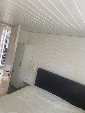 A bedroom with a bed, a wardrobe, a door, and a white ceiling with vertical lines.