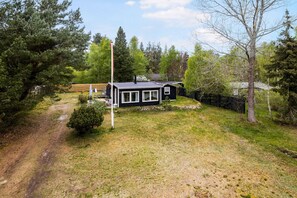 A small cabin with a sloped roof, surrounded by a grassy area and trees.