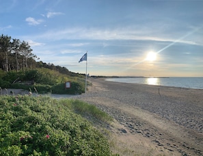 A beach with a flag, greenery, and a clear sky. - Summer house with terrace overlooking nature (Tikøb)