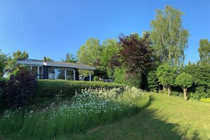 A modern house with a solar panel, surrounded by a well-maintained garden with white flowers and tall trees. - Summer house with terrace overlooking nature (Tikøb)