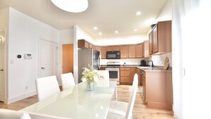 A modern kitchen with white cabinets, stainless steel appliances, and a dining area with a glass table and white chairs. - Harbor Escape- Minutes to beaches, Arts District, Harbor Shores & St Joseph (Benton Harbor)