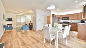 A modern living room with a fireplace, blue chairs, a dining table with white chairs, and a kitchen area with wooden cabinets and a microwave. - Harbor Escape- Minutes to beaches, Arts District, Harbor Shores & St Joseph (Benton Harbor)