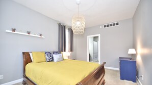 A bedroom with a wooden bed, a bedside table, a lamp, a shelf with decorative items, and a hanging light fixture. - Harbor Escape- Minutes to beaches, Arts District, Harbor Shores & St Joseph (Benton Harbor)