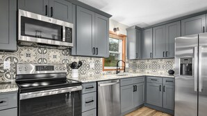 A modern kitchen with stainless steel appliances, grey cabinets, and patterned backsplash tiles. - NEW Breathtaking Views, Hot tub and Arcade, in a Peaceful Mountain View Retreat (Clyde)