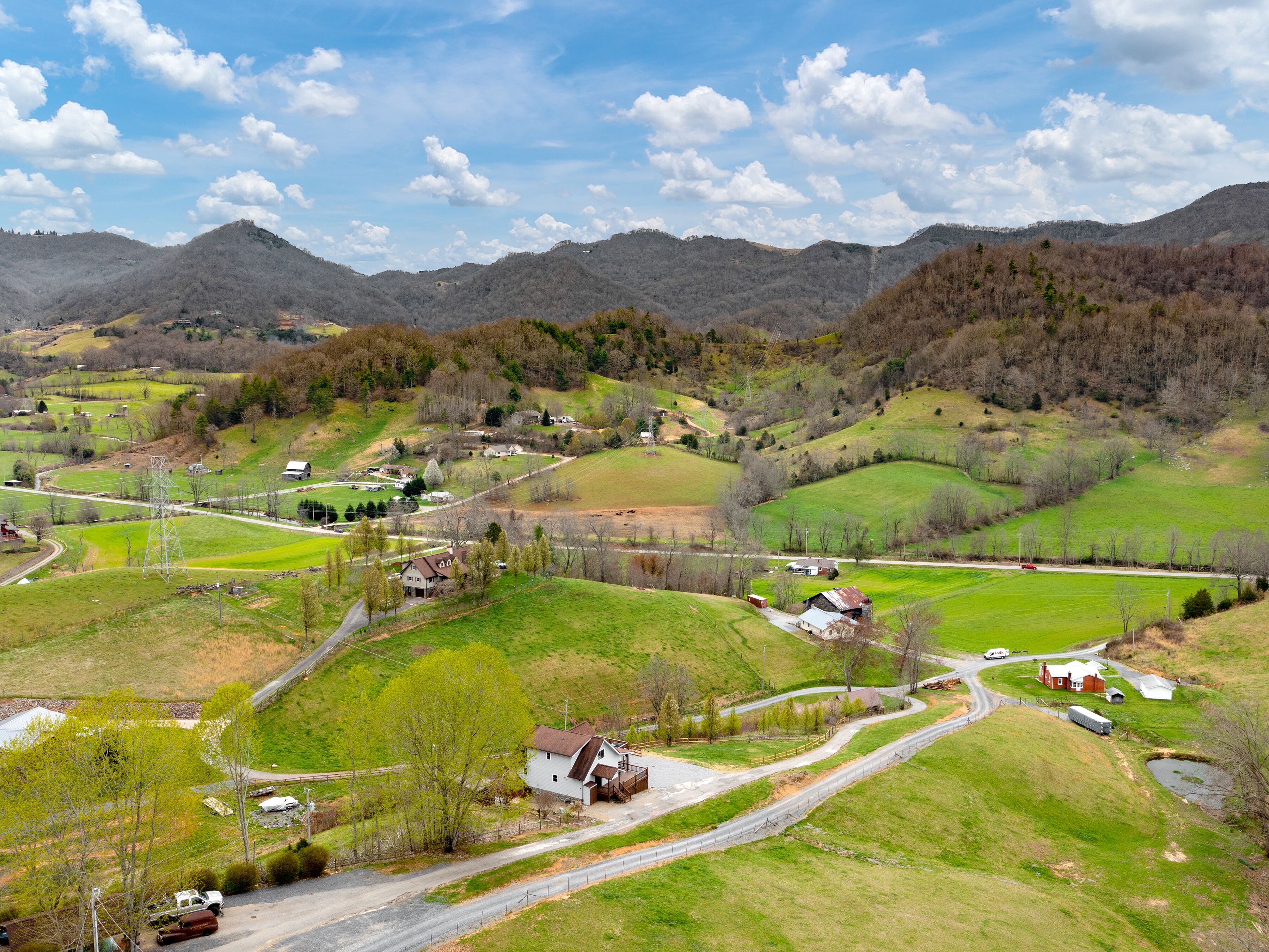 Een landelijk landschap met glooiende heuvels, een kronkelende weg en verspreide huizen.