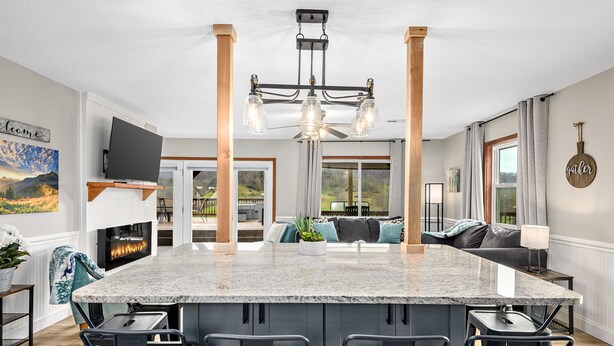 A modern kitchen with a central island, bar stools, a fireplace, and a view to an outdoor deck. - NEW Breathtaking Views, Hot tub and Arcade, in a Peaceful Mountain View Retreat (Clyde)