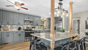 A modern kitchen with grey cabinets, a large island with bar stools, stainless steel appliances, and a ceiling fan. - NEW Breathtaking Views, Hot tub and Arcade, in a Peaceful Mountain View Retreat (Clyde)